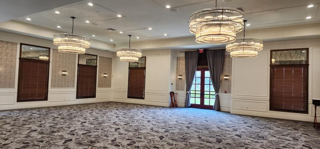 Spacious room with carpeted floor and chandeliers, featuring horizontal blinds.