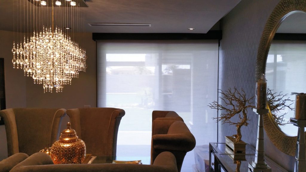 Elegant dining room with chandelier, mirror, and roller shades.