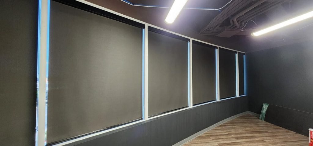 A room with black roller shades covering the windows and a wall with a floor.