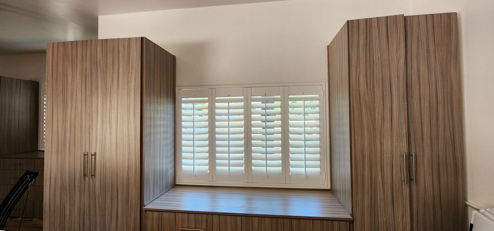 BROWN Elegant white plantation shutters framed by wood-grain cabinetry, creating a clean and balanced look in a modern bedroom or home office.
