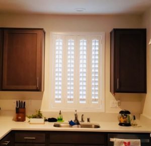 Modern kitchen with white plantation shutters on window above sink, providing light control and privacy.