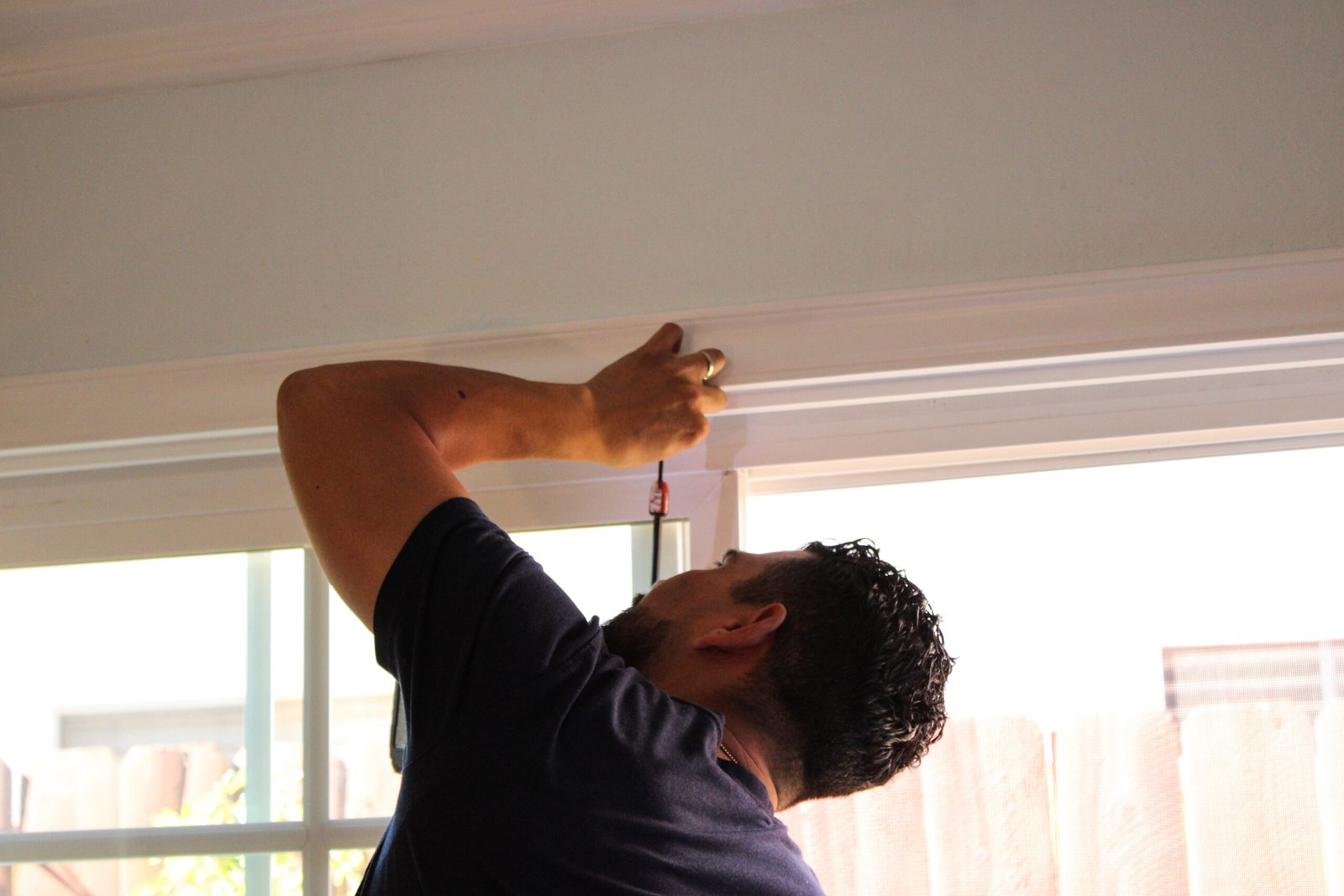 A professional installer mounting a window treatment inside a home, using a screwdriver to secure the top frame.