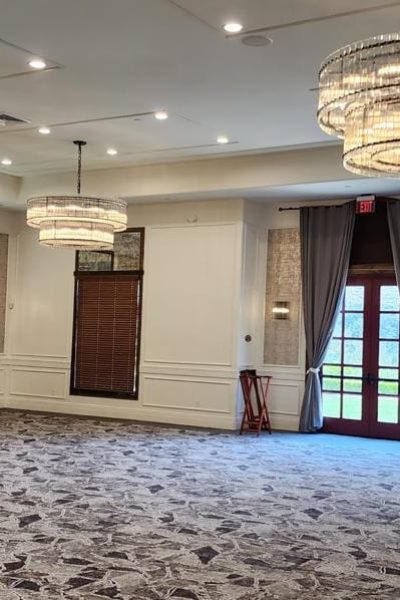 Spacious room with carpeted floor and chandeliers, featuring horizontal blinds.