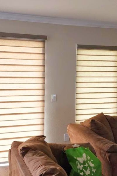 A cozy living room featuring a couch and a window with blinds and dual shades.