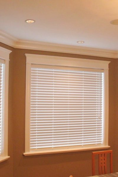 A dining room featuring three windows with horizontal blinds and a central table, creating a bright and inviting atmosphere.